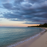 Serene tropical beach at dawn with clear ocean waves and distant palm trees, under a sky subtly transitioning from calm blue to atmospheric gray-blue clouds, hinting at the 2025 Atlantic hurricane season outlook and potential weather changes.