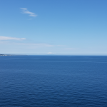 Serene Atlantic Ocean surface under a clear early June sky, with a faint, distant atmospheric swirl hinting at underlying forces, representing the quiet start to hurricane season contrasting with Pacific activity.